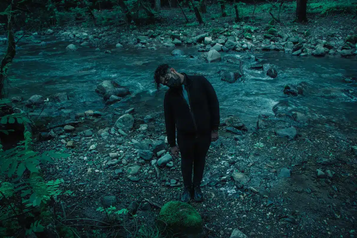 Un uomo cammina solitario attraverso un bosco scuro, trascinando un corpo verso un'ignota destinazione.