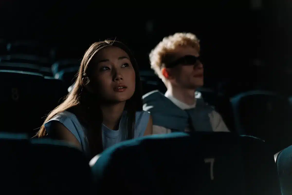 Persona seduta in sala cinematografica al buio, illuminata dalla luce dello schermo, con espressione di sorpresa e conte