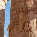 Interno di un'antica tomba egizia con geroglifici sulle pareti e manufatti dorati illuminati da luce ambrata
