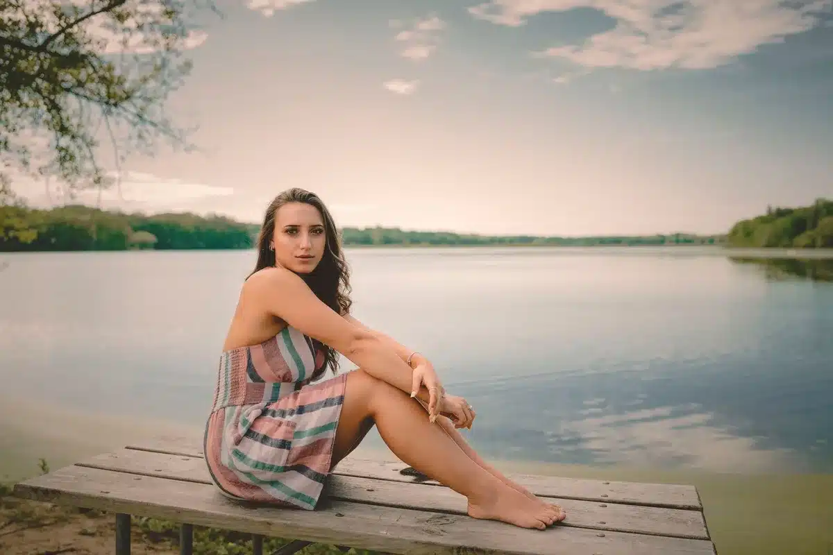 Una ragazza adolescente in piedi su un molo di un lago nebbioso all'alba, con una valigia ai piedi, che guarda verso la