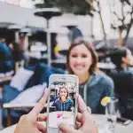 Due smartphone su un tavolo da caffè con mani silhouettate e folla sfocata sullo sfondo